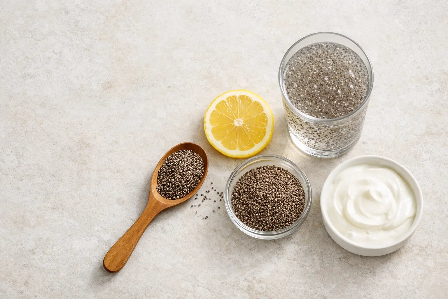 Chia seeds for weight loss—glass of chia water with gel, chia seeds, lemon slice, and Greek yogurt on a light stone surface.